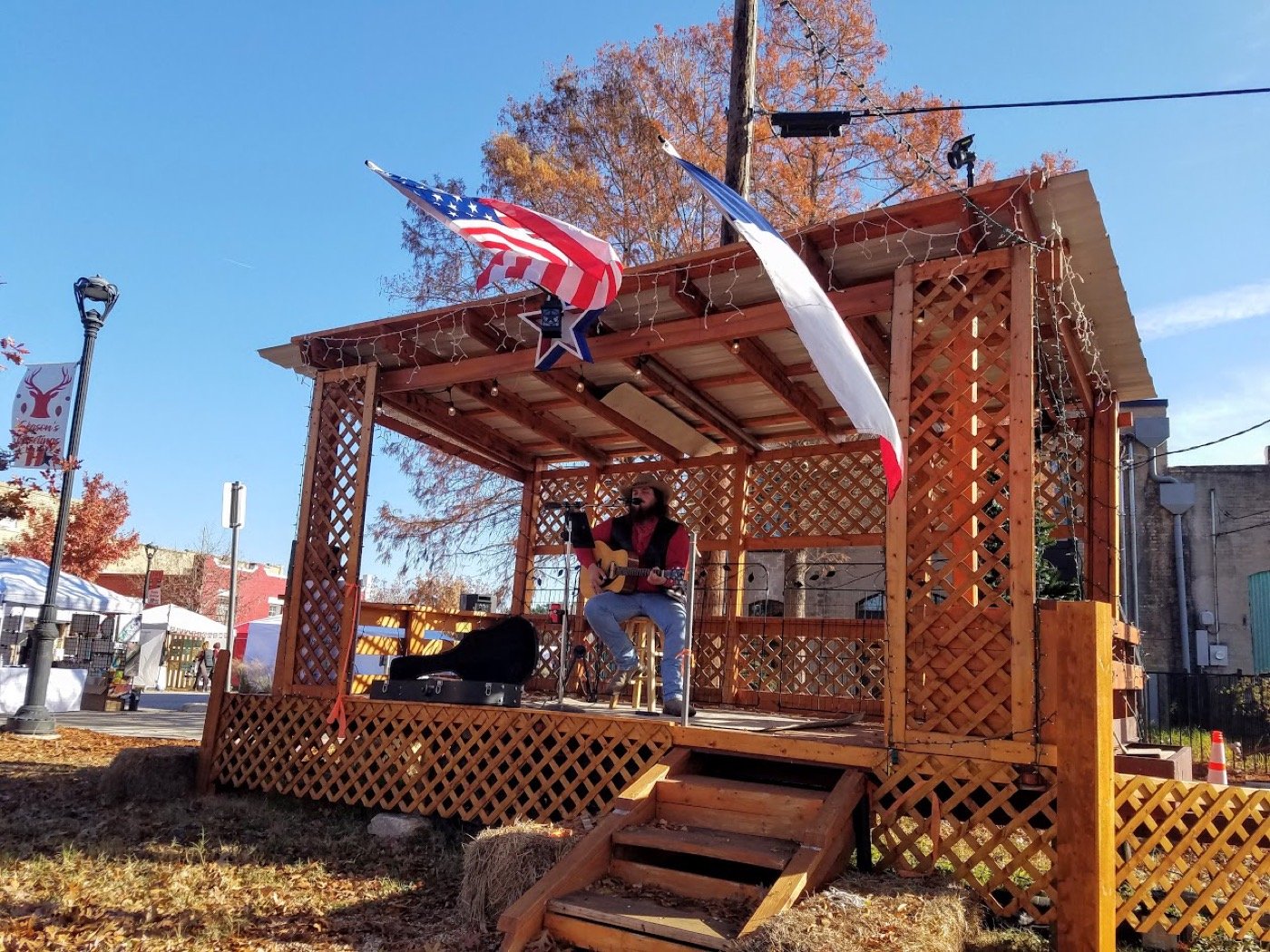 Acoustic set on a small wooden gazebo stage with a Texas flag on a clear fall afternoon.