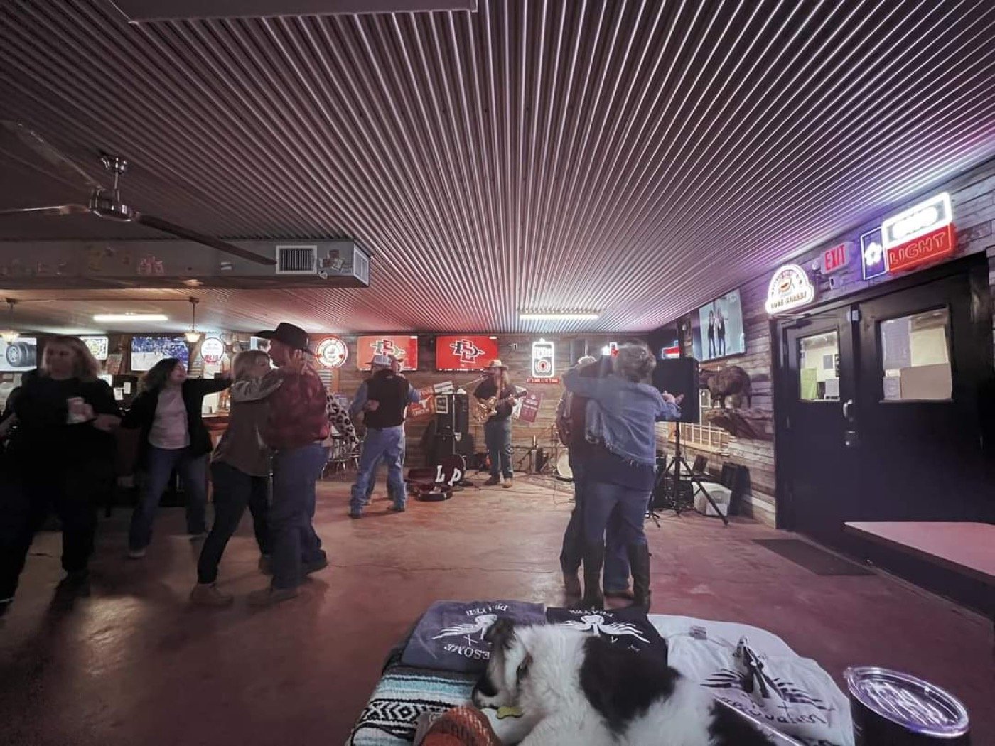Couples two-stepping on a dance hall floor while the band plays in the background.