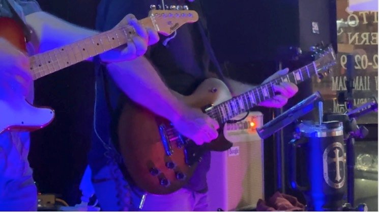 Close on two players' hands, a Telecaster and a Les Paul traded across the front of the stage.